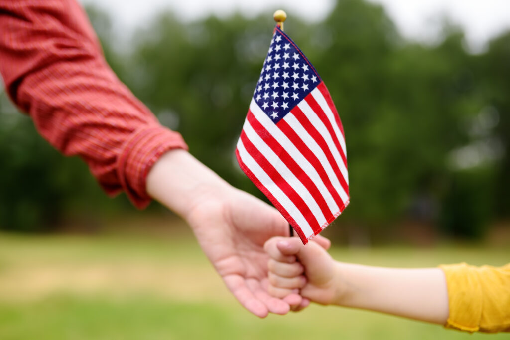mom and child holding hands and holding a small american flag in their hands