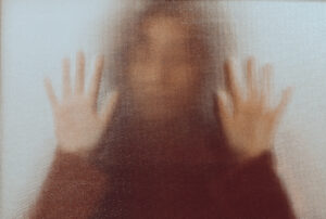 a woman behind an opaque glass, appearing trapped and wanting to escape.