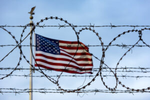 an American flag blowing in the breeze seen through barbed wire