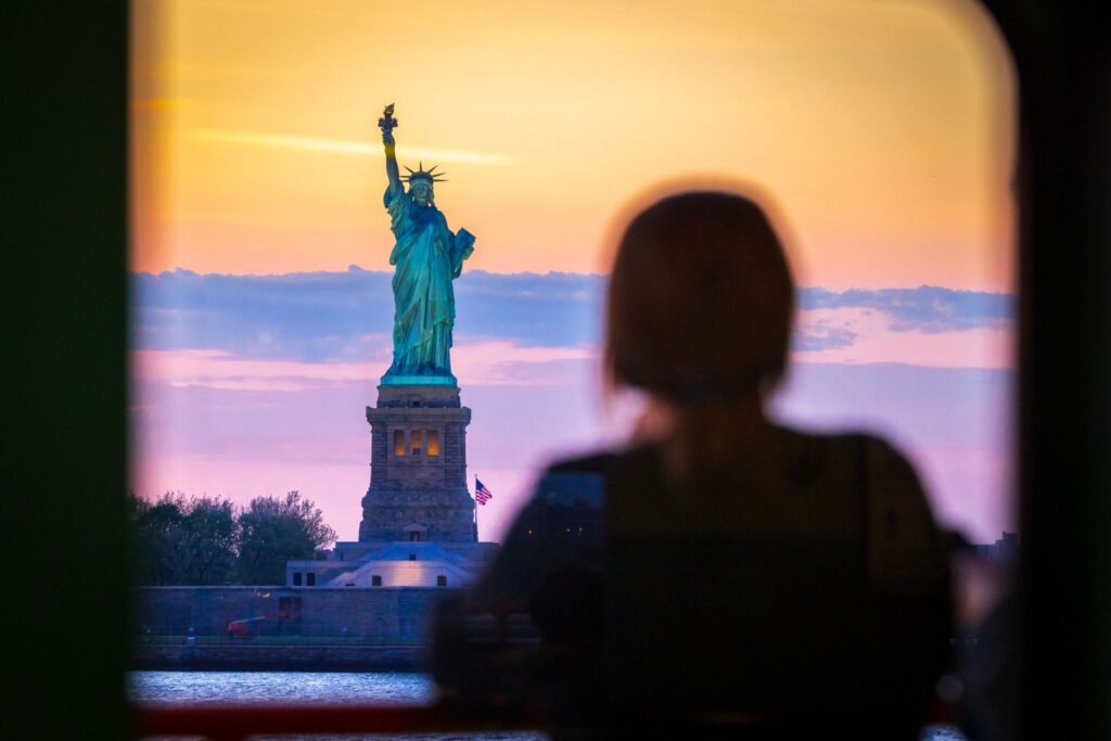 a person riding a ferry looks out the window at The Statue of Liberty.