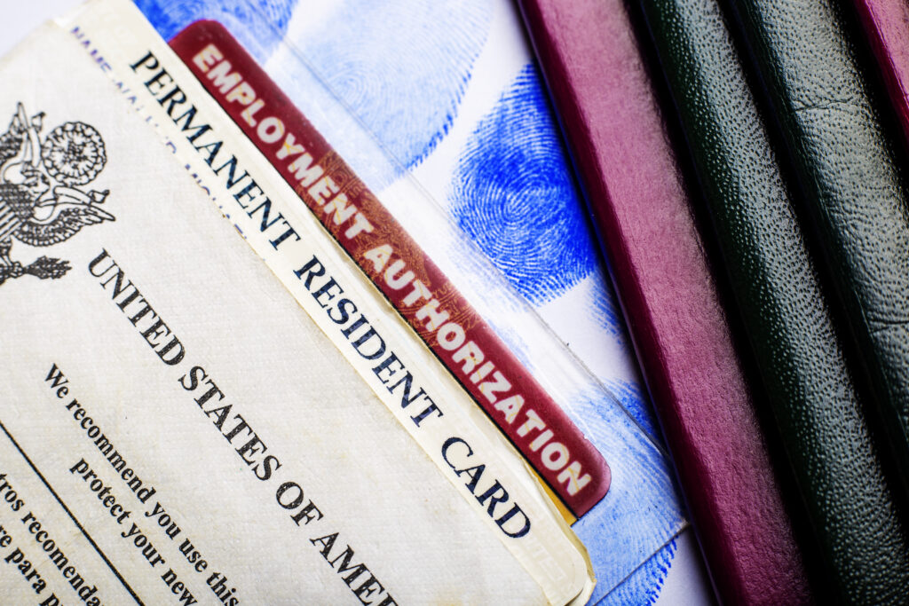 An employment authorization card on the bottom of a pile of US immigration cards and documents.