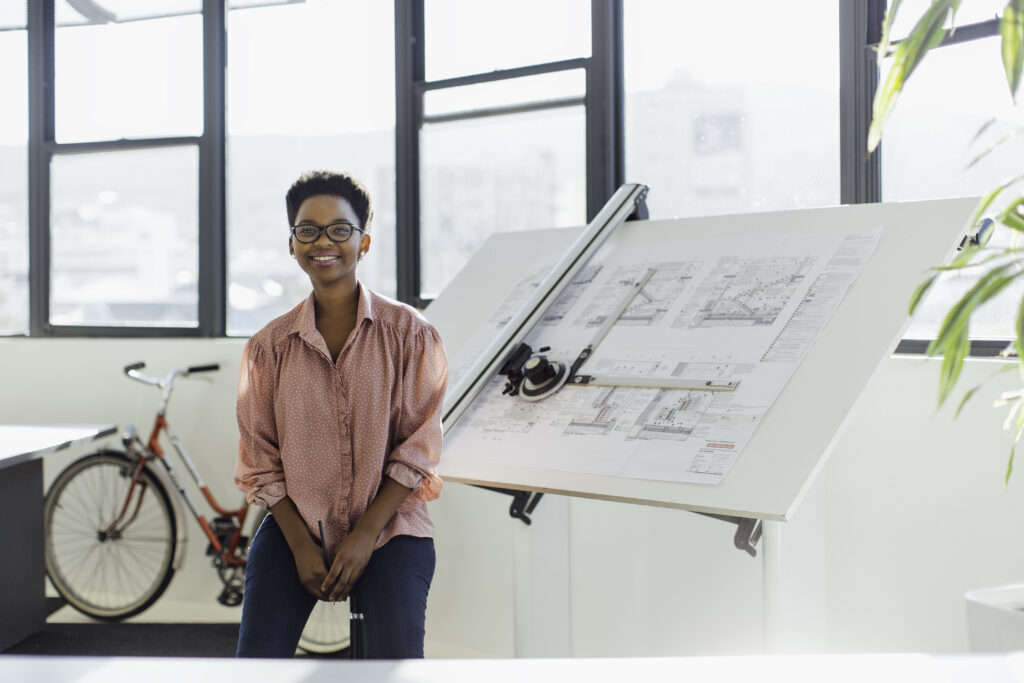 An architect sits next to a drawing board with architectural papers on display.