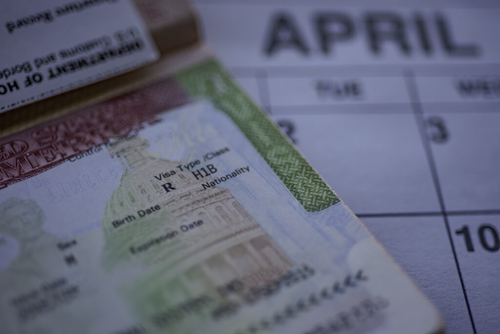 H1B visa (for specialty workers) stamp in passport, blurred april calendar on background. H1B visa program deadline concept. Close up of hb1 visa after bona fide termination