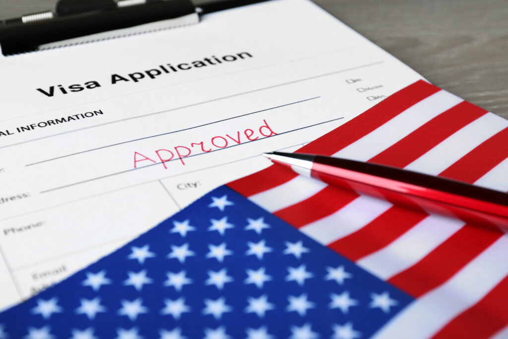 Visa application form with word Approved, American flag and pen on table, closeup