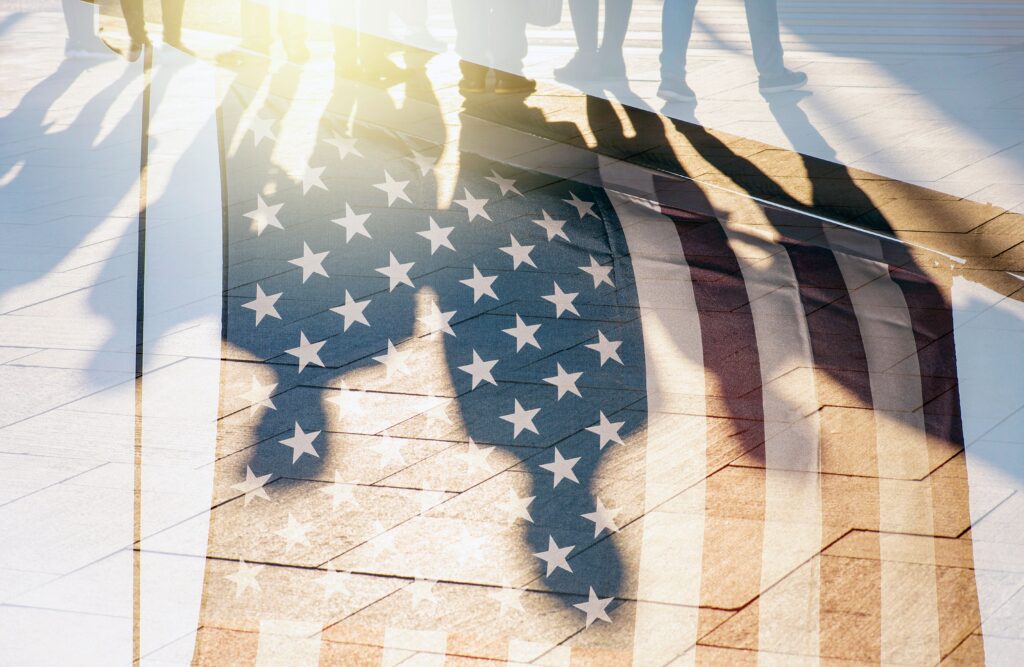 shadows of immigrants layered on an American flag